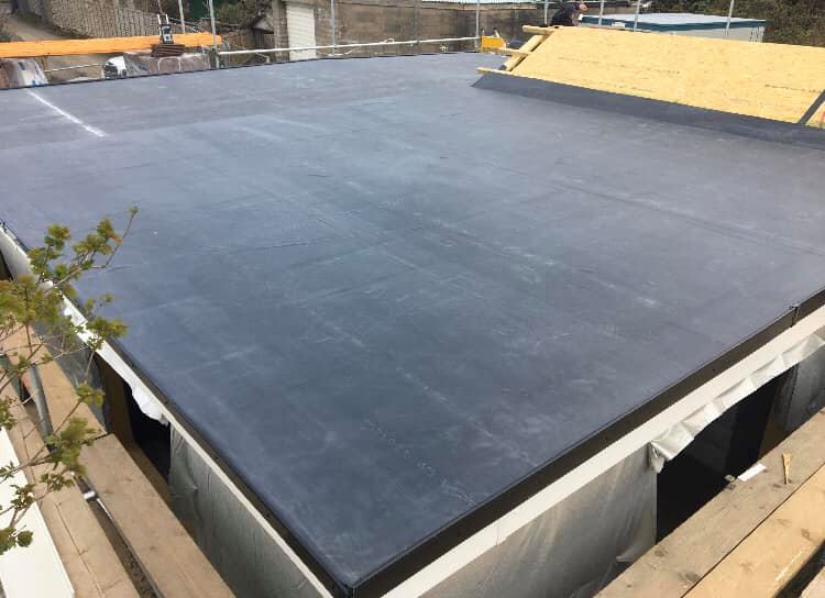 A newly fitted flat grey EPDM rubber roof covering a house extension, with scaffolding and roof timbers visible behind.